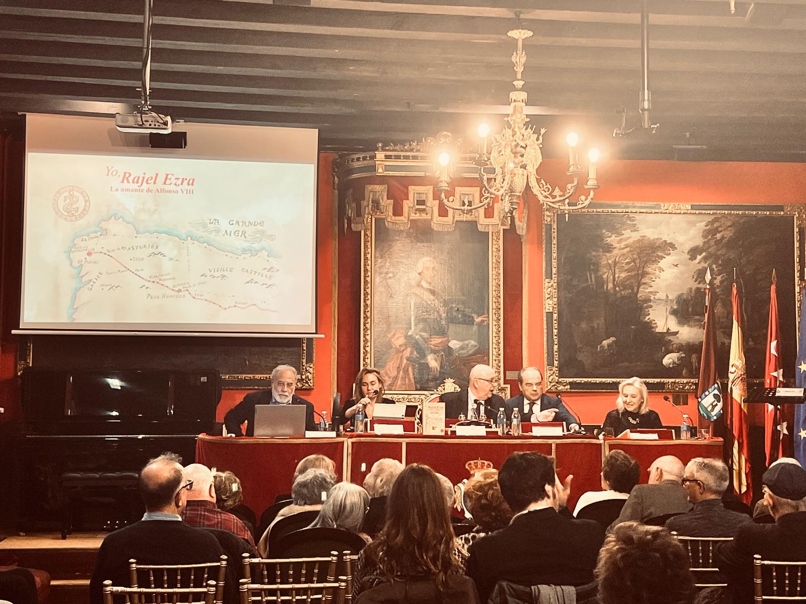 Fotografía horizontal de una presentación de libro con mesa presidencial, público asistente y pantalla de proyección en salón institucional.