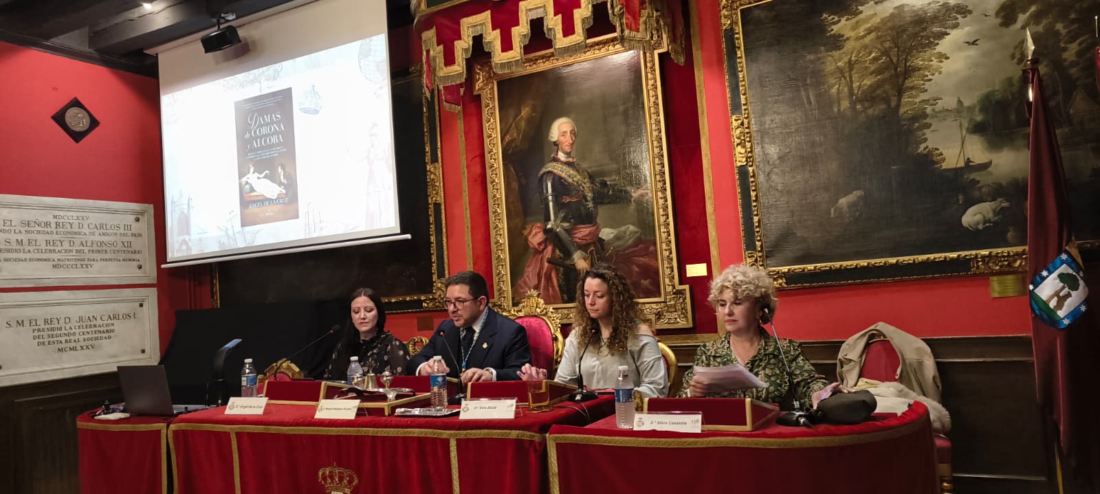 Fotografía horizontal de mesa de presentación con varios intervinientes en un salón de carácter histórico.