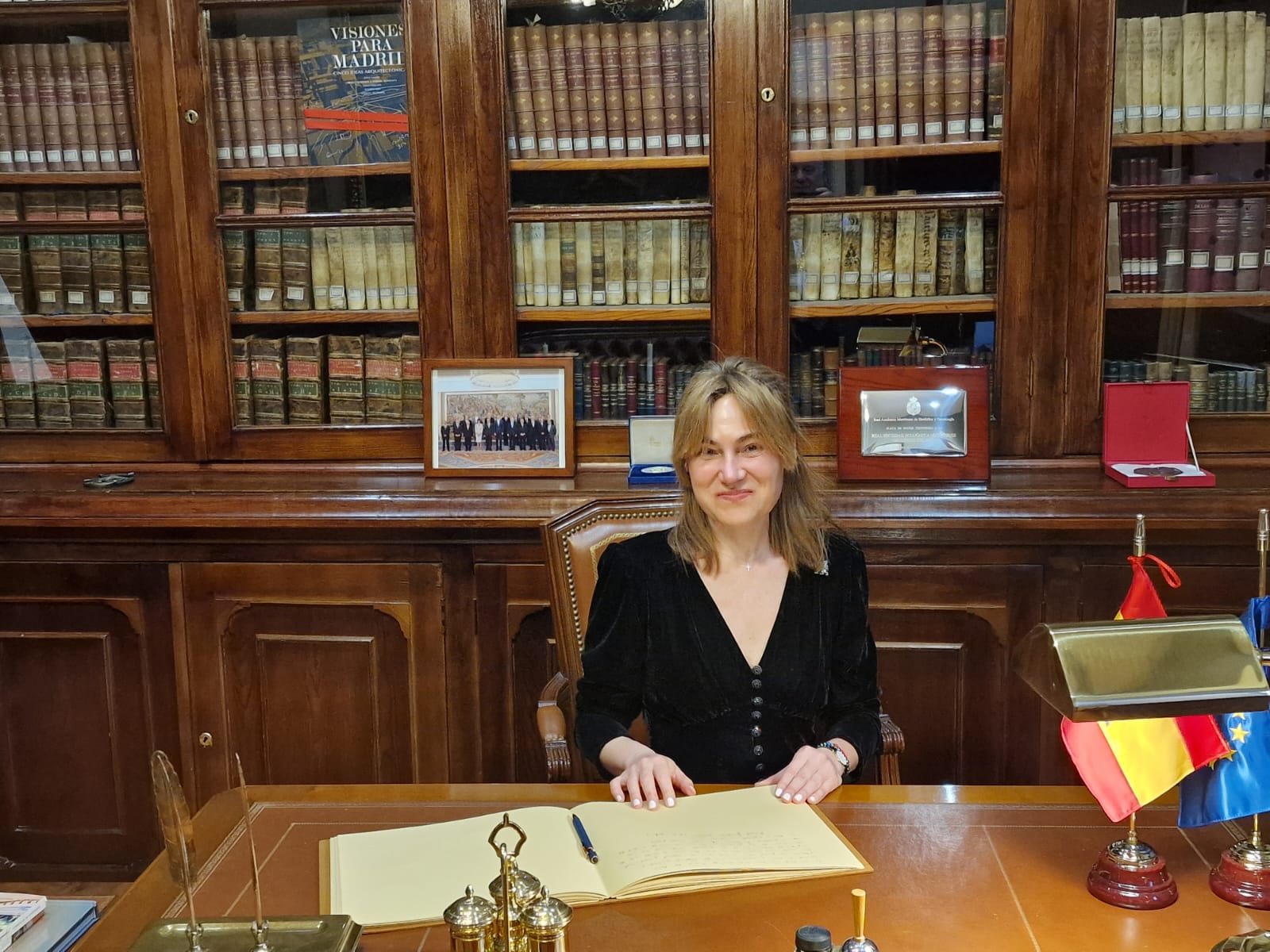 Fotografía horizontal de autora o invitada sentada ante una mesa de despacho con biblioteca histórica al fondo.