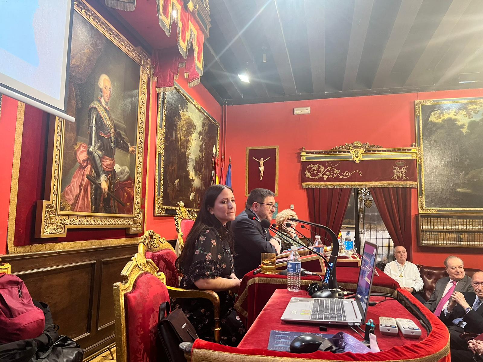 Fotografía horizontal lateral de mesa de ponentes en acto literario con asistentes y decoración histórica.