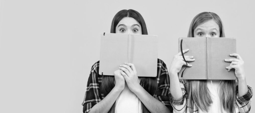Dos jóvenes sostienen libros abiertos frente al rostro durante una actividad de lectura