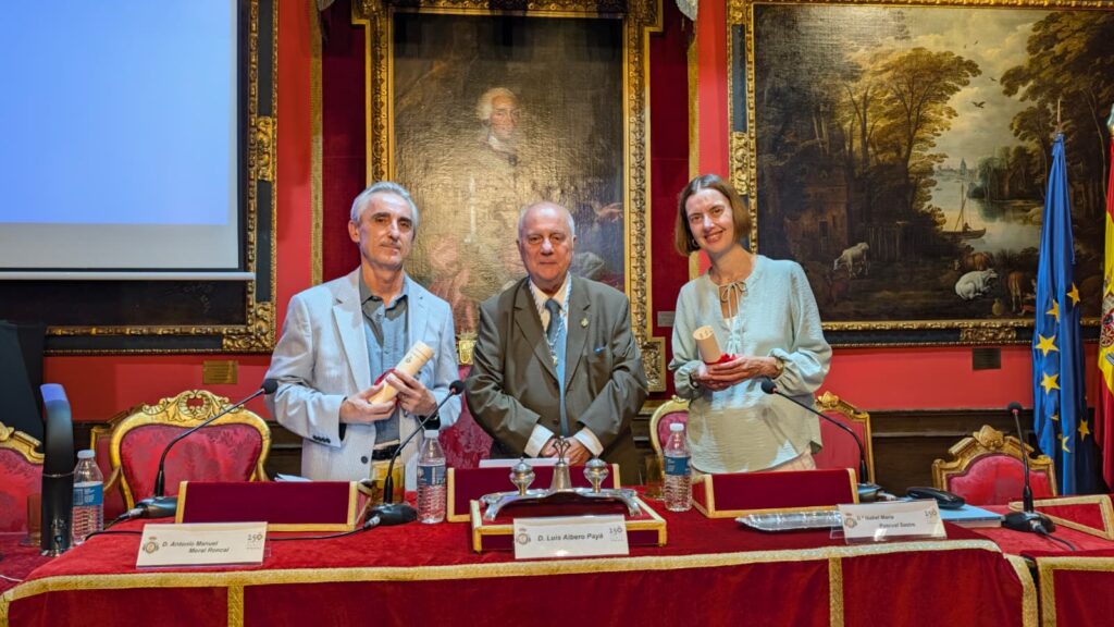 Tres participantes posan tras la mesa principal del acto Una infanta frente a Napoleon. Fotografia horizontal de tres participantes tras la mesa principal del acto Una infanta fren