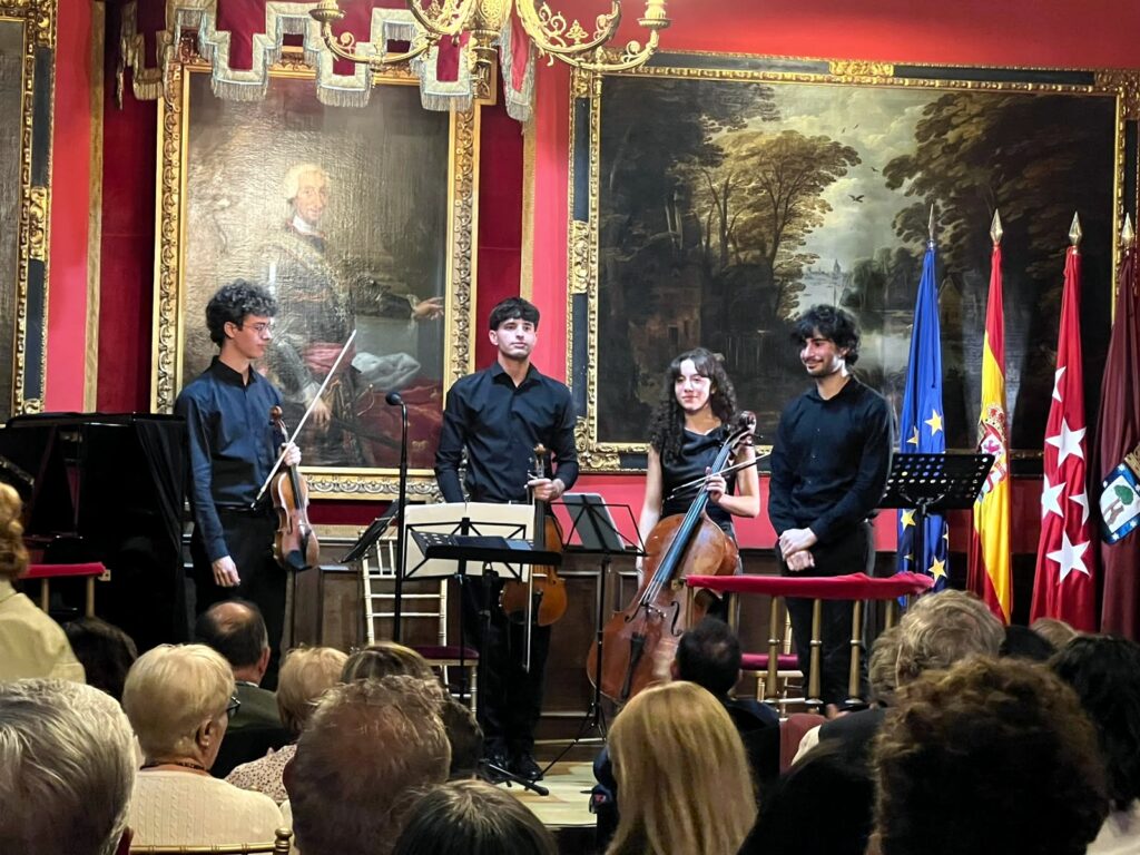 Fotografía horizontal tomada en el sal?n hist?rico de la Real Sociedad Econ?mica Matritense de Amigos del Pa?s, en Madrid. La imagen muestra a cuatro j?venes int?rpretes sobre el e