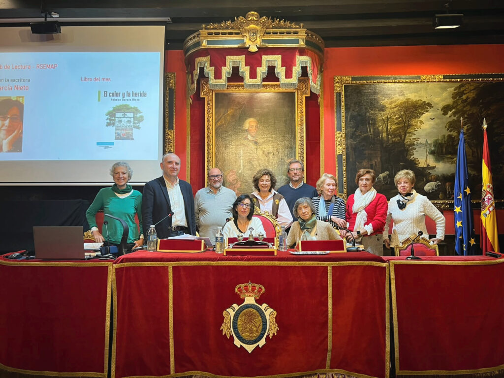 Grupo de asistentes posando en un salón histórico, junto a una pantalla que anuncia el libro «El color y la herida».