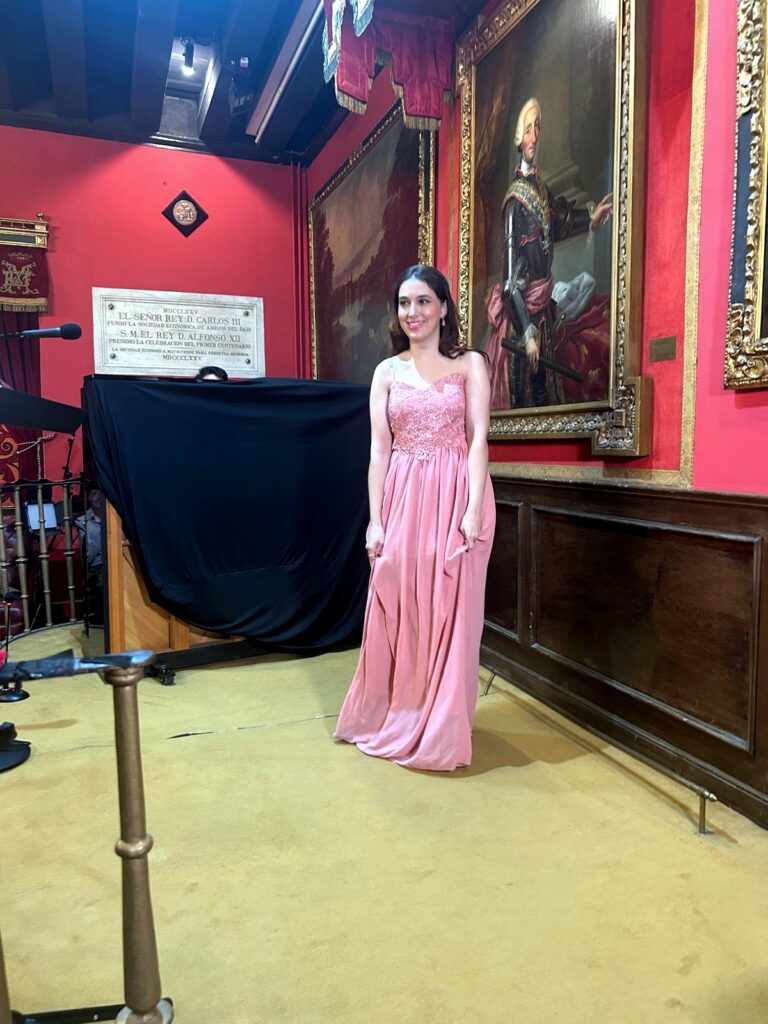 Fotograf?a vertical realizada en la Real Sociedad Econ?mica Matritense de Amigos del Pa?s, en Madrid. La escena recoge a una joven int?rprete con vestido largo rosa posando sobre e