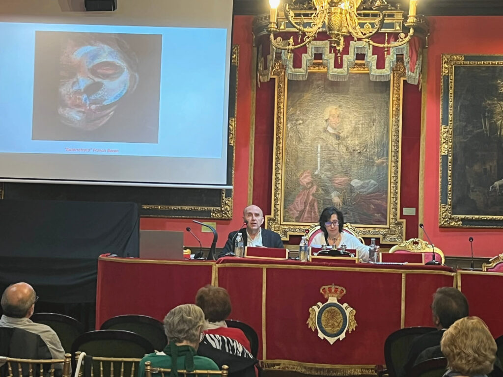 Un hombre interviene junto a una mujer ante el público, con un autorretrato de Francis Bacon proyectado en pantalla.