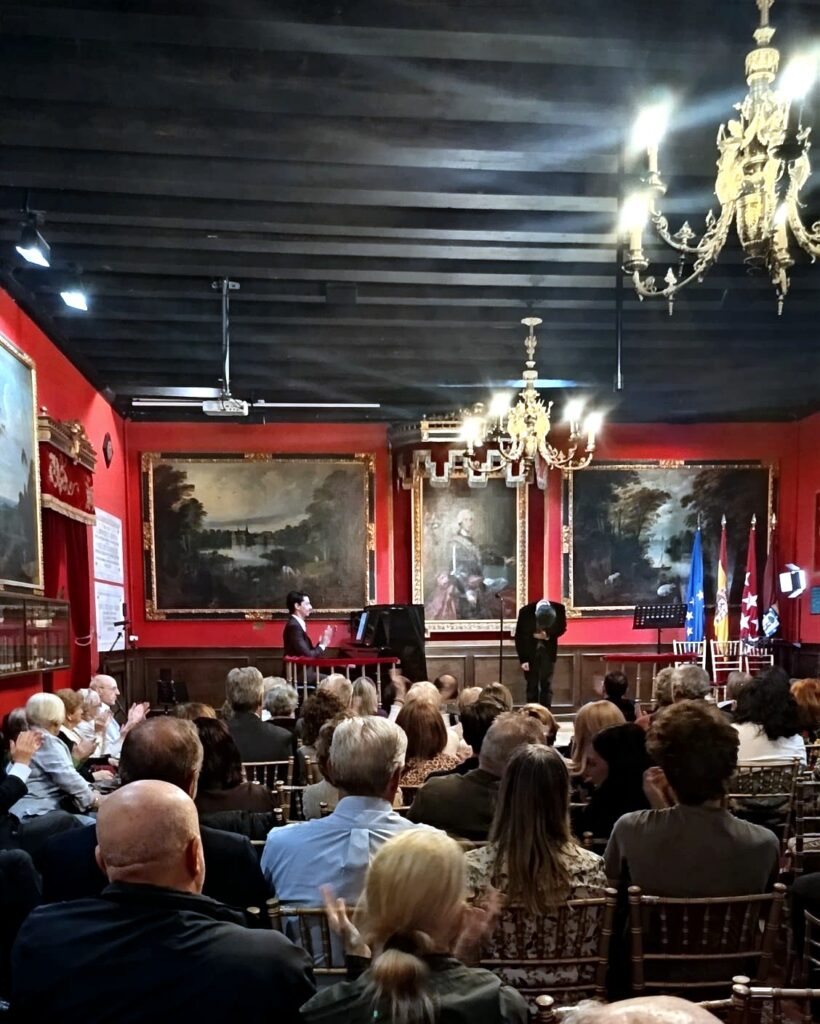 El p?blico aplaude al finalizar una actuaci?n musical en el sal?n hist?rico de la Real Sociedad Econ?mica Matritense, con el escenario y la decoraci?n institucional al fondo.