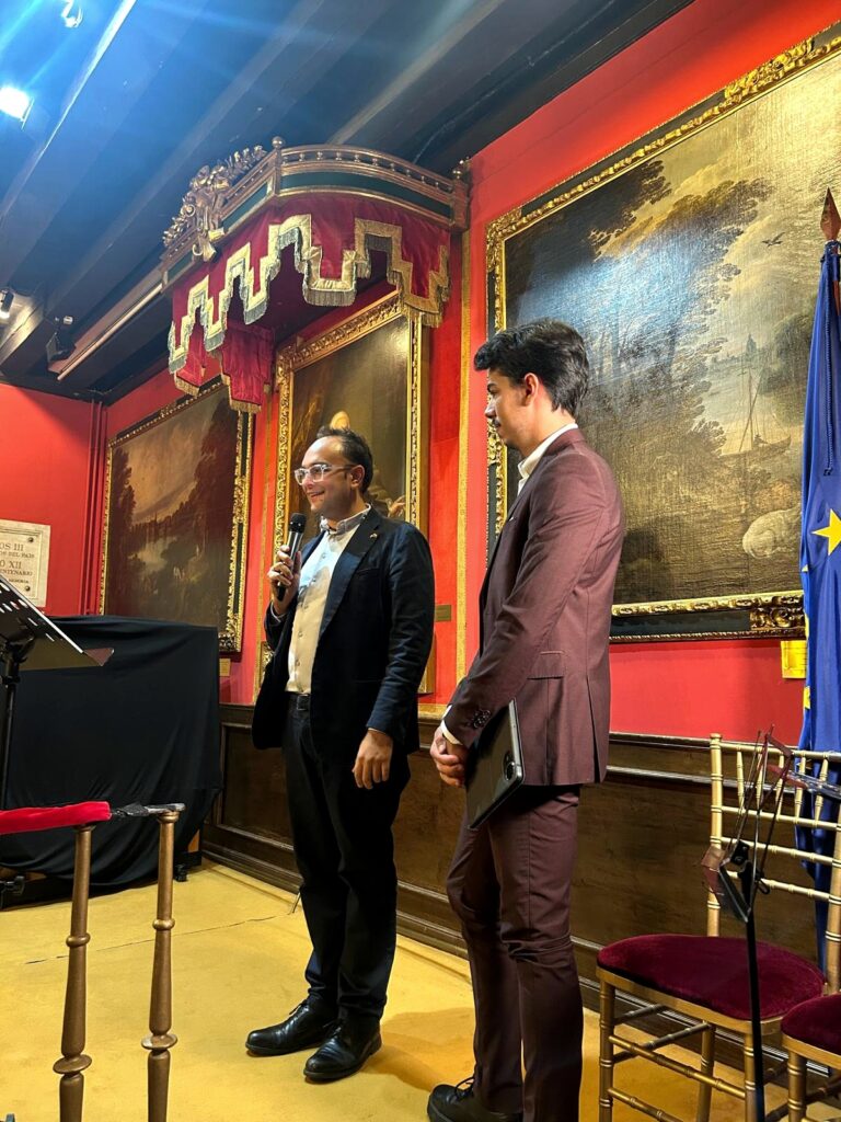 Fotograf?a vertical tomada en la Real Sociedad Econ?mica Matritense de Amigos del Pa?s, en Madrid. La imagen recoge a dos participantes de pie en el escenario, uno de ellos con mic