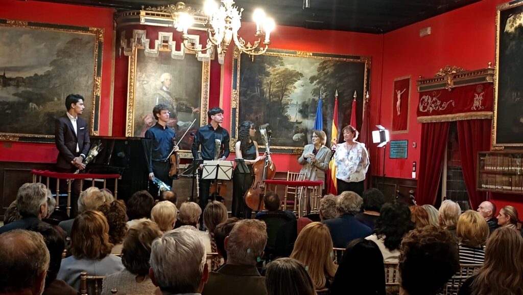 Fotografía del cierre de un acto cultural en la Real Sociedad Econ?mica Matritense, con m?sicos en el escenario, organizadoras del evento y p?blico asistente en la sala.