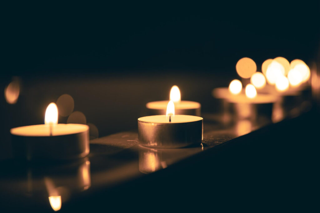 Velas de té encendidas alineadas sobre una superficie reflectante.