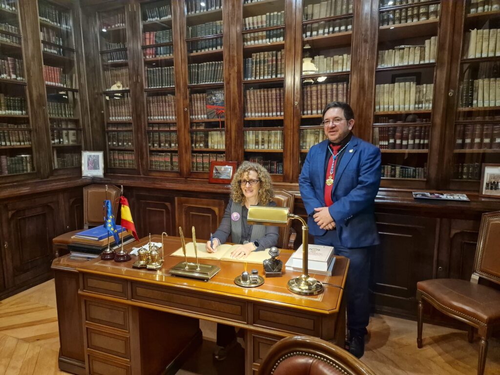 Imagen de recuerdo de dos participantes junto al libro institucional de la biblioteca de la Matritense.