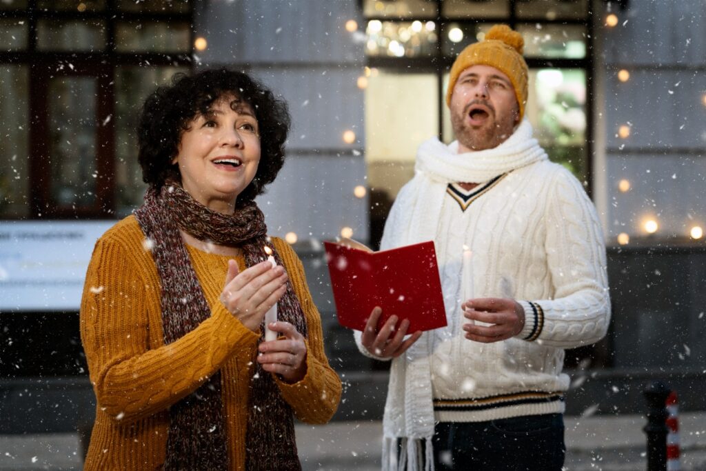 Dos personas con ropa de abrigo cantan bajo la nieve; una sostiene un libro rojo.