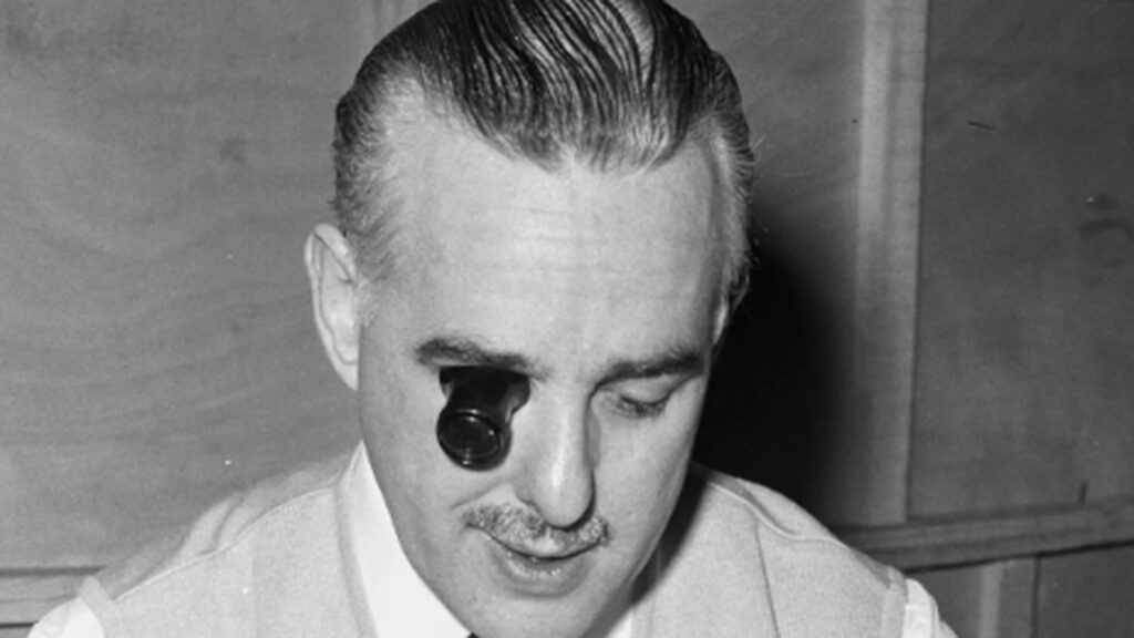 Hombre con una lupa monocular ante un ojo, retratado en blanco y negro.